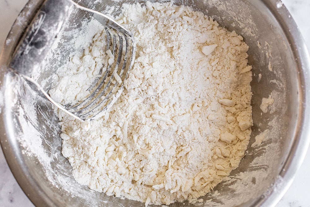 a bowl of the dry ingredients in this pie crust recipe, with the frozen shredded butter being cut in with a pastry blender.