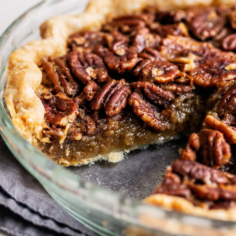 a pecan pie in a glass pie pan, with a slice taken out, showing the gooey nutty interior of the pie.