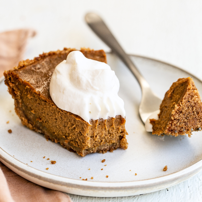 a slice of pumpkin pie with a dollop of whipped cream on top, sitting on a small plate, with a fork and a bite taken out.